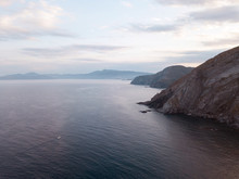 Aerial Top View Shot From Drone. The Speed Boat Rushes Over The Horizon On The Vast Mediterranean Sea Among The Majestic Stone Mountains And Blue Haze Covering The Sky. France, Port-Vendres.