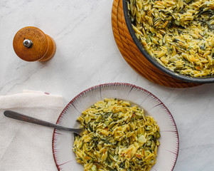 Poster - Orzo primavera with green veggies in vintage place over white marble table. One pot pasta with serving spoon, pepper grinder and napkin on set table. 