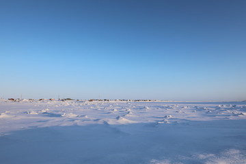 Wall Mural - Winter view of an isolated arctic community with snow and ice in the foreground and blue skies in the background, in Arviat, Nunavut Canada