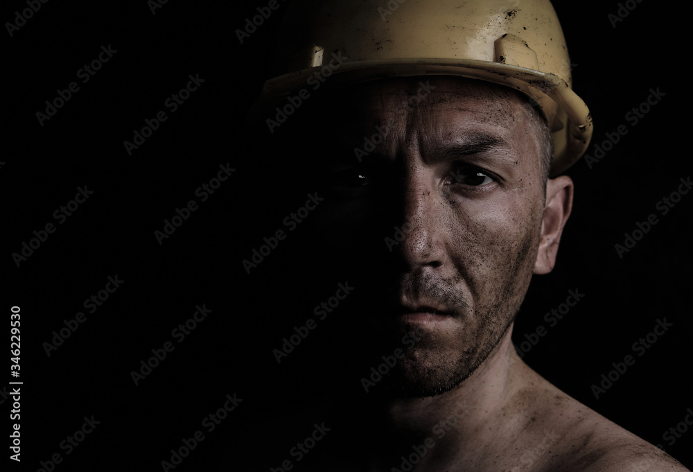 Miner in a yellow hard hat on a black background dirty with coal dust. - obrazy, fototapety, plakaty 