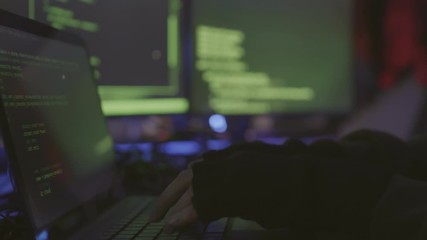 Close up of hands of unrecognizable coder sitting indoors in darkness and developing program code on different PC