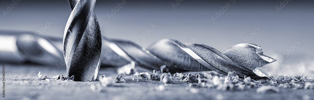 Drills from an electric drill lie on a board near the drilled hole. Joinery and construction work close up. Wood chippings fly off a metal drill. Panoramic banner. - obrazy, fototapety, plakaty 