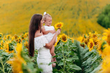 Wall Mural - Happy mother with the daughter in the field with sunflowers. mom and baby girl having fun outdoors. family concept. mother's day