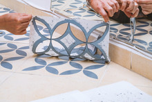Stay At Home And Home Improvement Concept: Close Up Of Hands Removing A Decorative Painting Stencil With A Vintage Design From The Floor Tiles After Successfully Painted Into Gray.