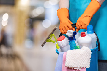 A bucket of cleaning products in hands with rubber gloves .