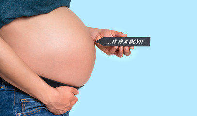 pregnant woman holding arrow with message IT'S A BOY in front of blue background