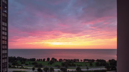 Wall Mural - An incredible aerial timelapse of a yellow pink purple and blue sunrise reflects on the water of Lake Michigan as it rises over the horizon with traffic zooming by on Lake Shore Drive below.