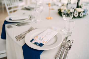 Wall Mural - Wedding dinner table reception. White plate on the table, three forks on the left, three knives on the right. The wedding menu is in the plate. Top view