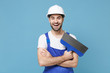 Cheerful young man in coveralls protective helmet hardhat hold putty knife isolated on blue wall background studio portrait. Instruments accessories for renovation apartment room. Repair home concept.