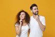 © ViDi Studio - Smiling pensive couple two friends european guy african american girl in white t-shirts posing isolated on yellow background. People lifestyle concept. Put hands prop up on chin, looking aside up.