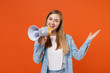 © ViDi Studio - Cheerful young woman girl in casual denim clothes posing isolated on orange wall background studio portrait. People lifestyle concept. Mock up copy space. Screaming in megaphone, spreading hands.