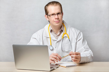 Telemedicine concept doctor man sitting at a table with a laptop.