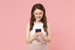 © ViDi Studio - Smiling young brunette woman girl in light casual clothes posing isolated on pastel pink wall background studio. People lifestyle concept. Mock up copy space. Using mobile phone, typing sms message.