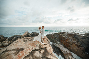 Wall Mural - beautiful gorgeous bride and stylish groom on a romantic moment stands on a cliff above the sea