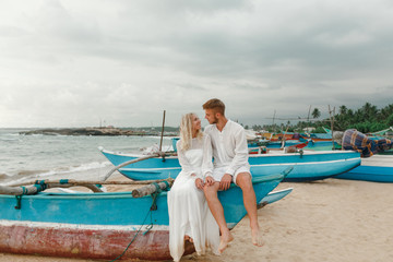 Stylish young bride and groom huging and kissing while sittin on traditional wooden boat in Sri Lanka