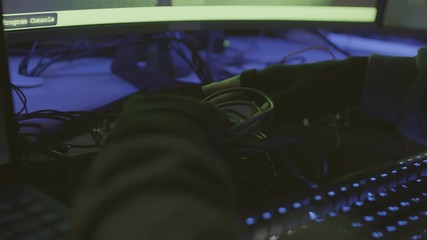 Rear view of hands of unrecognizable man sitting at desk at computer and untangling black wires