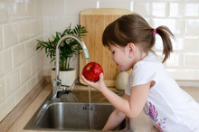 Girl Washes A Red Apple In The Kitchen Near The Sink. The Concept Of Children's Health And Independence