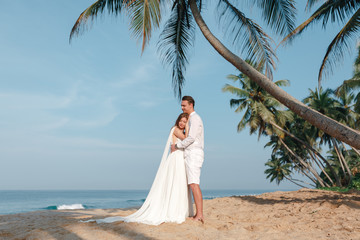 Wall Mural - Bride and groom with palm trees on a tropical beach. Wedding by the sea