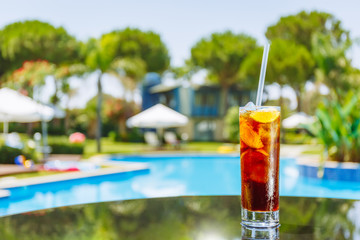 Wall Mural - Glass of cuba libre cocktail on the glass table near swimming pool. Luxury vacation concept. Horizontal