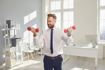 Happy successful businessman in a white shirt does exercises with dumbbells in the office.