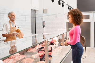 Wall Mural - Lady choosing raw meat behind counter.