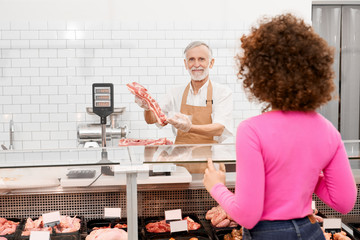 Wall Mural - Male butcher demonstrating meat in supermarket.