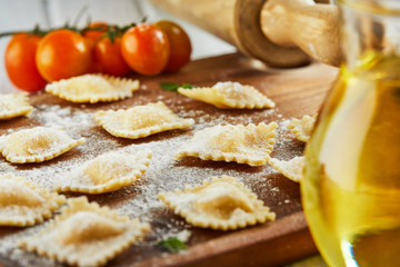 Wall Mural - Tasty raw ravioli with flour, cherry tomatoes, sunflower oil and basil on a light wooden background. The process of making Italian ravioli.