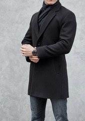 Wall Mural - man stands wearing black coat at gray background. young man in classic clothes.