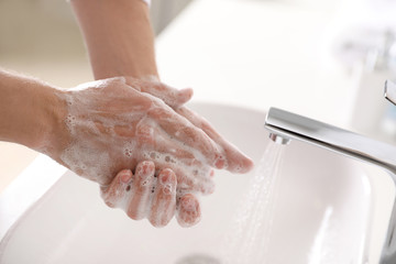 Man washing hands with soap over sink in bathroom, closeup