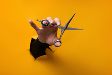Hairdresser Holding In Hand Scissors For Cutting Hair From A Torn Hole In Orange Paper