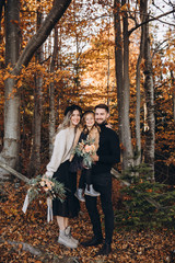 Wall Mural - Stylish family in the autumn forest. A young guy and a girl are standing near a wooden fence and holding their daughter in their arms. Mom and daughter are holding bouquets of flowers