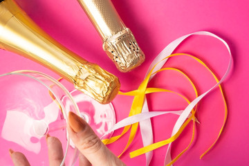 Two champagne wine bottle neck in gold silver foil,near champagne glass and colored satin ribbons on bright pink, flat lay top view. Concept of celebrating, birthday, congratulations, happiness, party