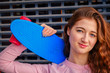 The red-haired girl looks straight into the camera with a slight sneering smile while her long red hair is strewn over her shoulders which rests her blue skateboard with red wheels
