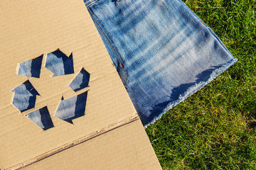 Wall Mural - Recycle symbol on denim fabric over green grass. New skirt from old boyfriend jeans