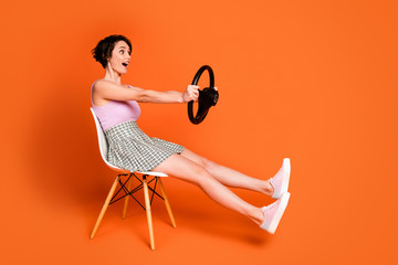 Sticker - Full length profile side photo astonished positive girl sit chair hold steering wheel imagine she drive fast automobile wear checkered pink singlet isolated bright shine color background