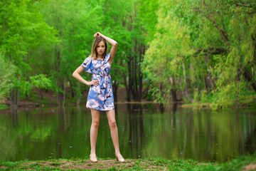 Portrait of a young beautiful woman in blue dress posing by the lake