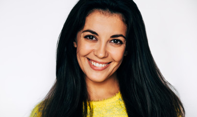 Studio closeup shot of charming young female wears yellow jumper, smiling and looking to the camera, isolated over white background.