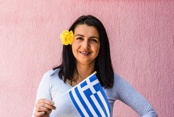 Wall Mural - Woman holds flag of Greece  in front of isolated wall background