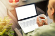 © ronstik - woman drinking tea and using laptop on a outdoor terrace, blank screen copy space