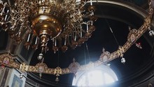 A Large Golden Chandelier With Many Yellow Bulbs Hanging From The Ceiling And Illuminating A Dark Gloomy Church With A Large Altar, Close-up, Bottom View