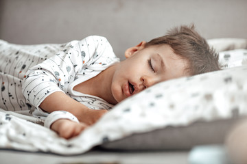 Wall Mural - Cute little boy sleeping. Tired child taking a nap in parent's bed. Clean, fresh and cozy bedding sheets. Bedtime for kids. Sleepy toddler boy sleeping on his bed