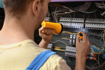 Poster - Male electrician with flashlight repairing distribution board