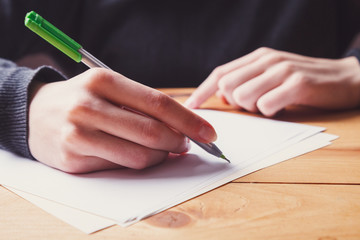 Wall Mural - young woman hands writing notes on sheet of paper with pen closeup, wooden table, female student