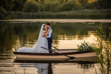 Fototapeta  - young beautiful newlywed couple sit in wooden white boat