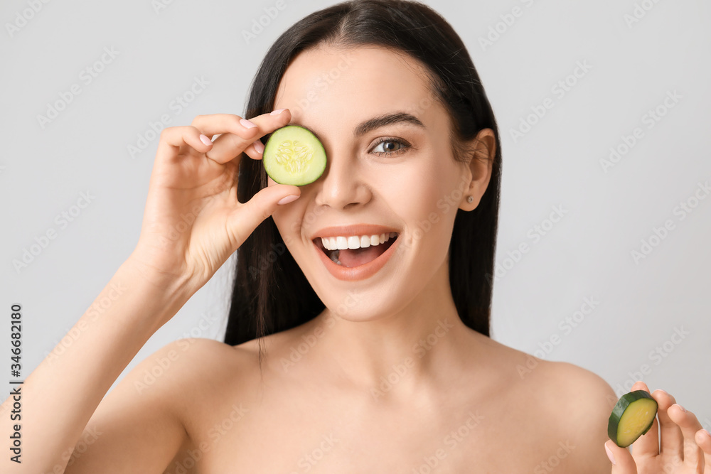 Beautiful young woman with cucumber slices on light background