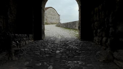 Wall Mural - Entering on arched tunnel gate of medieval fortress with old stone walls in Berat Albania, drone dolly shot