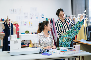 Wall Mural - Two fashion designers women looking at piece of dress and checking mistakes. young girl coworkers discussing together with new season collection in workshop. group of female tailors working in studio