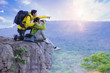 © Panumas - Couples hikers use binoculars to watching the view, sitting on top of the hill enjoy with nature