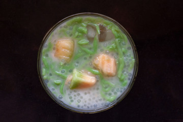 Top view of Thai pandan short vermicelli with piece cantaloupe in Coconut Milk, Thai people call Lod Chong in bowl on black tile background.