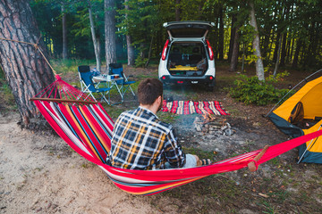 Wall Mural - man laying on hammock at lake beach near camp fire